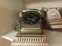 Photo showing vintage rotary phone with coiled cord, rotary dial, and push-button line selector. Also shows Bates Space Saver Under-Phone Index box in background.