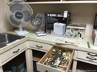 Full lot view showing breadmaker box, two fans, cappuccino maker, and drawer with scissors.