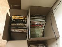 Two cardboard boxes filled with assorted records and sheet music, showing a sizable collection of vintage music items.