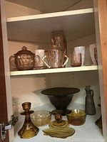 Shelf with pink and amber glassware, rose colored covered dish, and tumblers visible