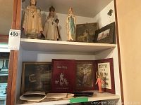 Display of three Paris-made religious figurines and framed pictures on a shelf.