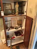 Image showing religious items arranged inside a cabinet including statue, crosses, framed prayers, and rosary.