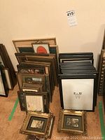 View of multiple picture frames stacked together on the floor, showing variety in designs and images inside some frames.