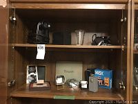 Shelf containing various vintage photographic items including Kodak splicer, cameras, slide projector, and glass fluid.