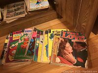 Photo showing a spread of vintage comic books and magazines lined up on floor with visible colorful covers, including True Love Pictorial and Walt Disney comics