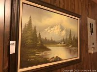 Full view of original framed oil painting showing mountain landscape with lake, trees, and cabins.