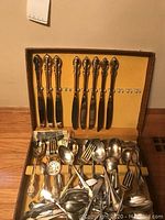 Photo of the wooden case with knives hung on hooks and assorted cutlery arranged in the bottom compartment