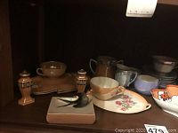 Full view of top shelf with two small beige salt and pepper shakers, butterfly serving dish, floral tray, bird figure, and lustre ware teacup.