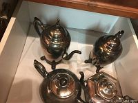 Four pieces in the silver plated coffee and tea set arranged in an open drawer.