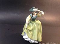 Front view of the Royal Doulton Buttercup figurine showing the woman in her traditional dress holding her hat.