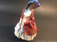 Front angle showing the woman figurine in detailed dress and hat with label attached.