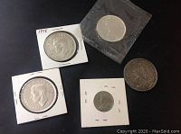 Overview of four coins on black background: top left 1938 Voyageur dollar in holder, top right 1964 Charlottetown commemorative dollar in plastic pouch, bottom right Queen Victoria silver crown 1891, bottom center King George V five cent piece 1922 in holder