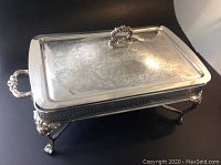Full view of rectangular silver plated centrepiece with lid closed, showing ornate handle and detailed engraving on lid, and side handles.