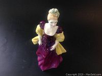 Top angled view of Royal Doulton Loretta figurine in purple dress, yellow shawl, detailing facial features and hair.