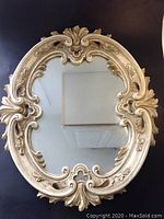 Full front view of ornate oval mirror showing detailed molded plaster frame with scrolling and leaf motifs.