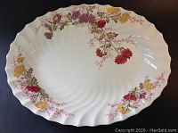 Top view of oval-shaped porcelain serving platter with scalloped edges and floral pattern in multicolor tones.
