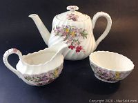 Teapot, creamer, and sugar bowl tea set with floral Fairy Dell pattern on white porcelain, showing front and side views.
