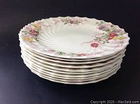 Stack of ten large dinner plates with floral pattern on white ceramic showing wavy edges.