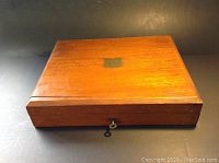 Closed wooden flatware case with brass plaque on top.