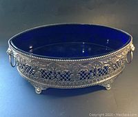 Front and side view of oval centrepiece showing pierced and embossed copper exterior with decorative handles and indigo glass liner