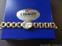 Tissot ladies watch placed on original blue box with silver logo. Shows full bracelet and dial.