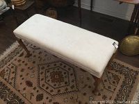Top view of long queen anne style bench showing white upholstered seat on hardwood frame and legs.