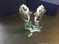 Pair of clear Swarovski crystal seahorses standing on a shared blue-tinted crystal base, shown with open Swarovski blue box in background.