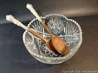 Cut crystal salad bowl with scalloped edge and starburst cut patterns, holding two servers with olive wood ends and silver handles.
