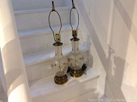Pair of tall crystal vase lamps on white stairs, showing overall condition and size.