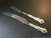 Carving knife and fork laid out to show full length of blade and tines, and sterling silver Louis XV style handles.