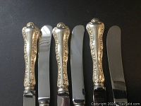 Six butter knives arranged side by side on black background, showing handles and blades.