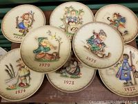 Photo showing the eight vintage Goebel Hummel plates with various year markings and hand-painted figures.