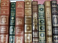 Books arranged in two rows showing the variety of titles and leather bindings in brown, green, burgundy colors with gilt decorations on spines.