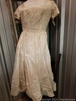 Full length photo of cream vintage wedding dress with lace bodice and tea-length satin skirt hanging in a closet.