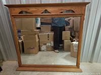 Large oak vanity mirror with three arch cutouts at the top and rectangular mirror, placed against a wall with boxes in background.