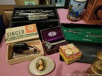Photo of assorted vintage items showing Singer Blind Stitch Attachment, compasses, a small decorative item with Mona Lisa image, and a purple jewelry box.