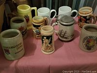 Overview of nine assorted vintage beer steins on table, various sizes and designs including German-themed and Seton Hall.