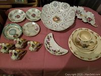 Overview of assorted vintage china including four plates, four teacups with grapevine and gold detailing, a white pierced bowl, two decorative dishes with floral designs.