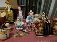 Wide view of assorted vintage figurines including several clowns, a cat creamer, dog bookends, and a small white vase.