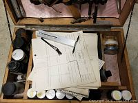 Top view of wooden fingerprint kit box interior showing fingerprint powder jars, brushes, tools, and papers.