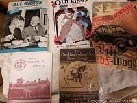 Photo showing vintage magazines and pamphlets including 'All Hands', 'Old King's Variety Show', Franklin D. Roosevelt pamphlet, 'The One Hundred and One Best Songs' songbook, and a KdF-Wagen poster.