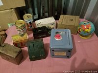 Overview of the 11 vintage metal banks arranged on a table including combination lock safe, perpetual calendar, house shapes, and advertising cans.