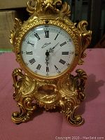 Front view showing decorative brass clock with white dial and Roman numerals.