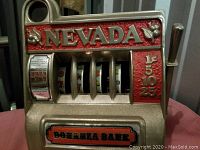 Front view of the vintage cast iron slot machine bank with visible 'Nevada' text, slot reels, coin values, and lever.