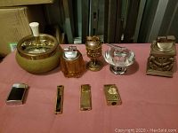 Complete view of vintage cigarette lighters and ashtray arranged on pink fabric surface
