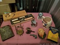 Full view of the vintage assorted items on a pink cloth, showcasing curling iron box, candle holder, miniatures, stein, figurine head, tin, and other small items.