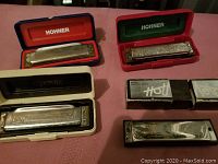 Four harmonicas on pink cloth include three in Hohner hard cases and one in original Hot Metal box