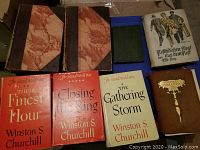Photo showing two large vintage marbled hardcover books with brown spines, three red dustjacketed Winston Churchill WWII books, a green book, an illustrated book on Nottinghamshire Essex Sussex, and one brown hardcover titled Michael Quadland.