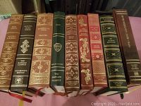 Front spines of nine leather bound books including titles like Honoré Balzac, Canterbury Tales, The Study of My Life, and Of Human Bondage, showing detail of embossed gold decoration and ribbon bookmarks.