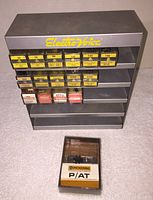 Full view of metal Electro-Voice display rack with multiple rows of vintage needle cartridge boxes, plus one separate Pickering cartridge in plastic box.